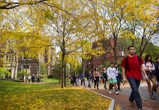 Students walk across a college campus in the fall.