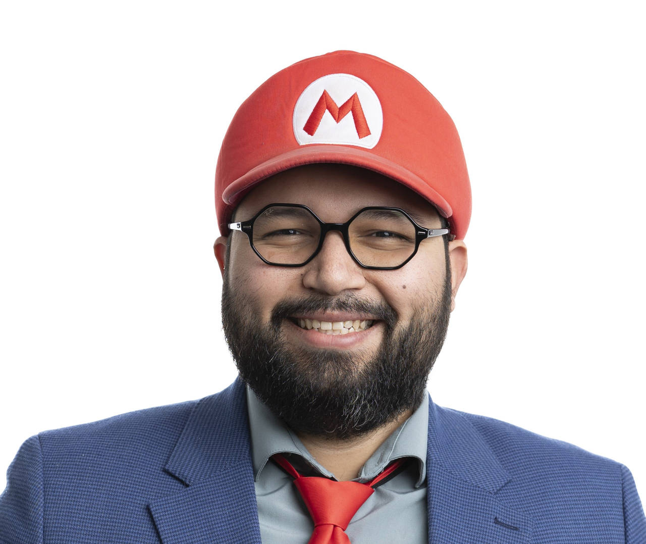 Person wearing a red Mario-style cap, blue suit jacket, gray shirt, and red tie, photographed against a white background