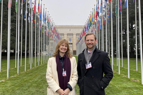 Two people standing in front of rows of flags