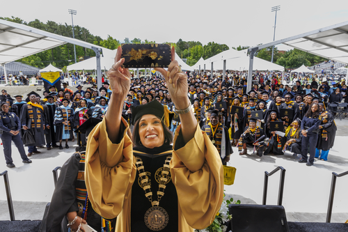 President Breaux dressed in graduation regalia takes a selfie from the stage at Commencement in front of all the students in their caps and gowns.
