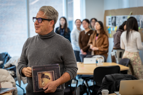 Gerald Campano holds a book and students in his class are visible in a crowd behind him. 