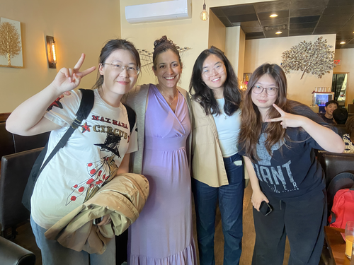 Four women pose together smiling. Two of them give peace signs with their fingers. 