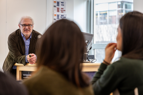 Dr. Supovitz leans over a table, engaged with his students who are talking to him. 
