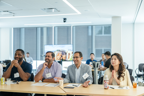 A row of four alumni judges wearing nametags with a screen and a window behind them. 