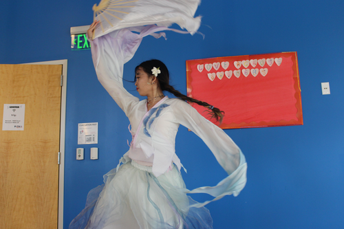 A woman in a flowy white costume performs a dance inside a community center.