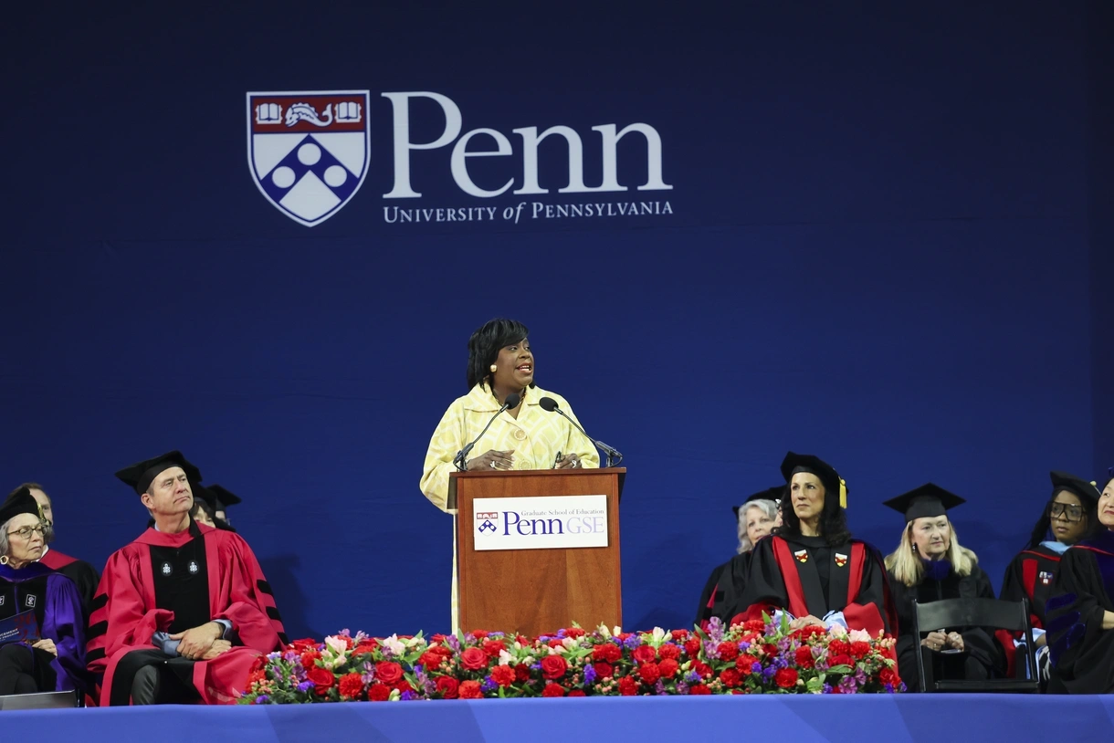 Mayor Cherelle Parker speaks at a podium while Dean Katharine O. Strunk and other faculty in regalia look on at Penn GSE's 2024 commencement ceremony