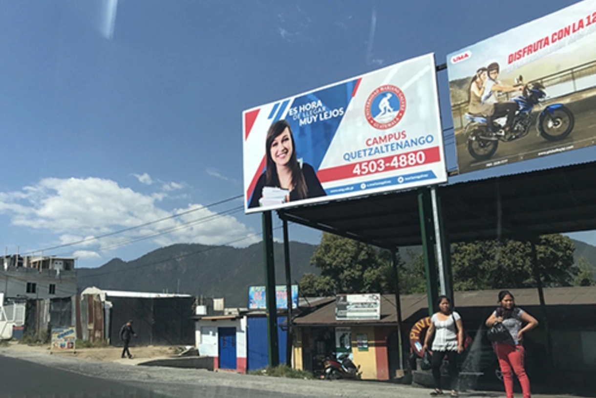 Women waiting for the bus below an ad for a private university.