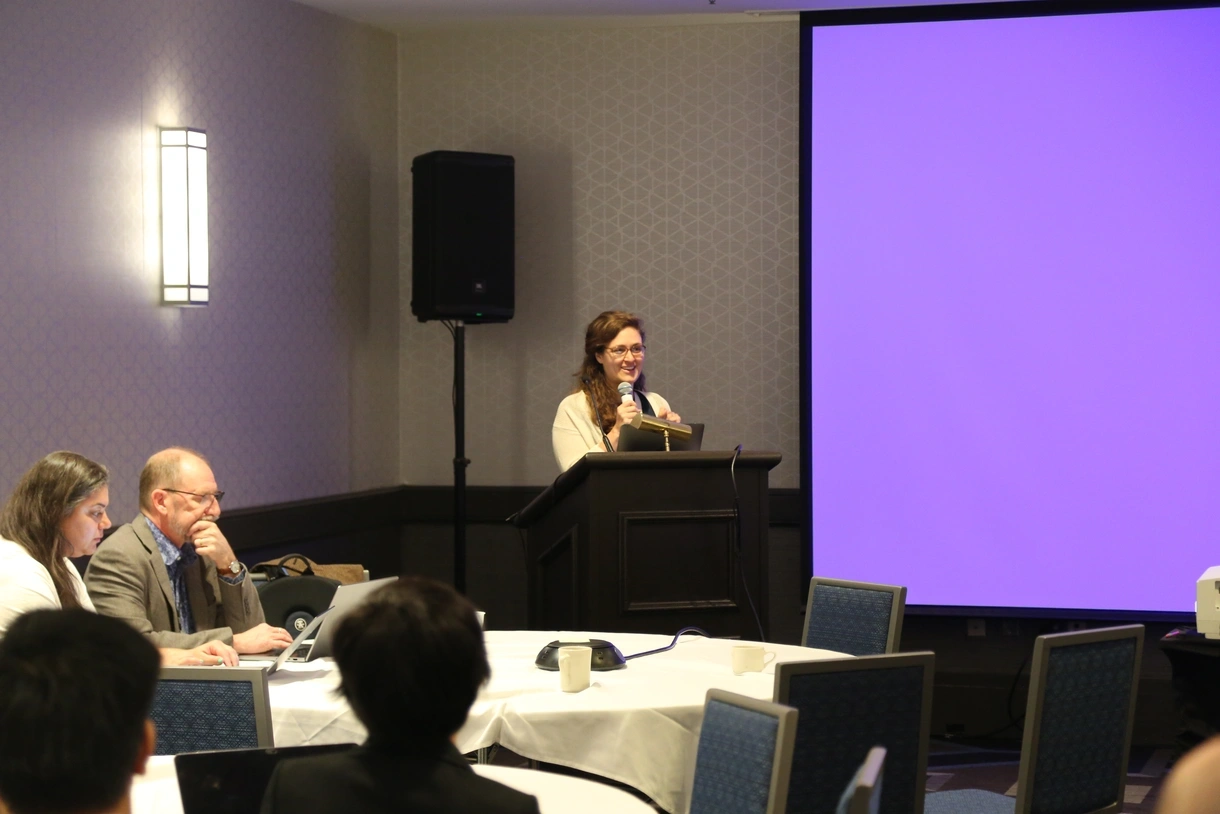 Amanda Barany speaks into a microphone in front of a crowd at ICQE.