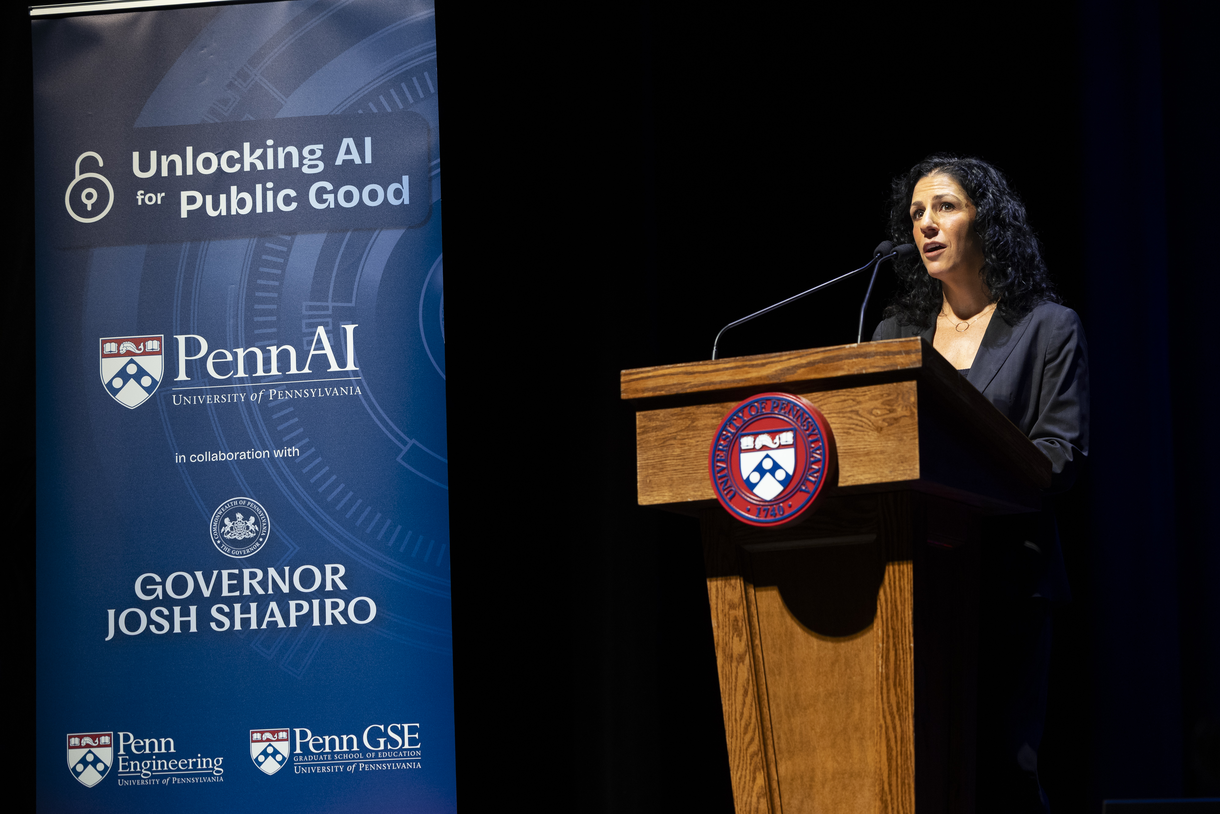 Dean Strunk speaks at a podium with a Penn seal on its front and next to a banner that reads "Unlocking AI for Public Good" with logos from PennAI, Governor Shapiro's office, Penn GSE, and Penn Engineering on it. 