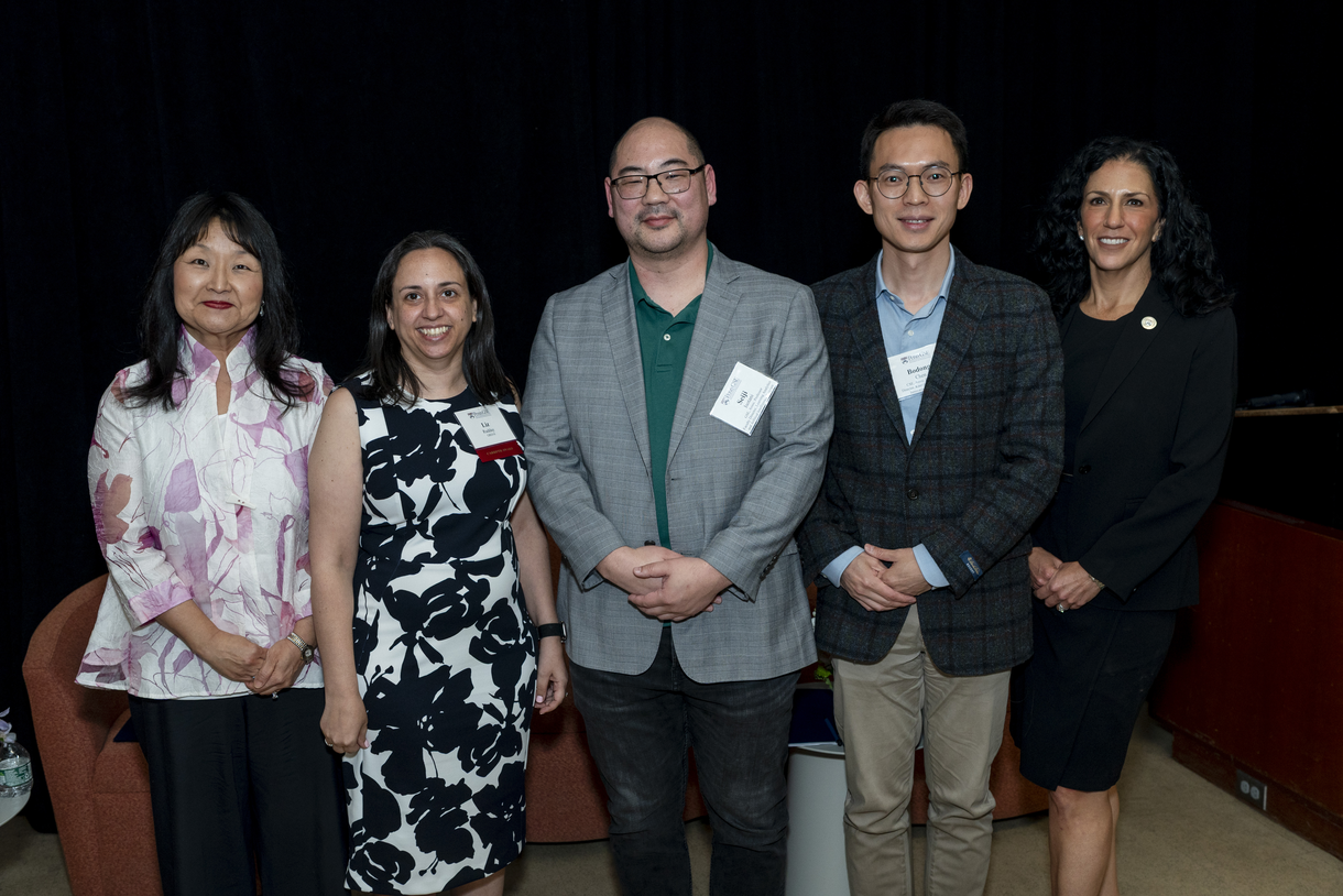 The four panelists and the dean stand in a row, posing for a portrait and smiling. 