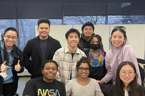 Nine teenage members of the CARE Initiative sitting and standing together in a classroom, smiling.