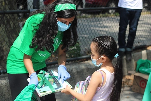 Rina Madhani showing a package of books to a small child.