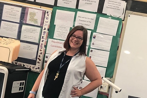 Sarah Cannon-Straight stands in a classroom in front of a bulletin board.