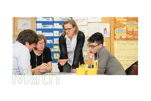 Three students work together in a classroom as a faculty member talks to them