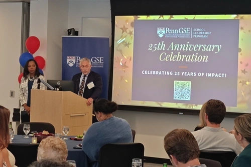 Steve Piltch and Jessica Richard address a seated crowd from behind a podium with a screen behind them reading "Penn GSE School Leadership Program 25th Anniversary Celebration"