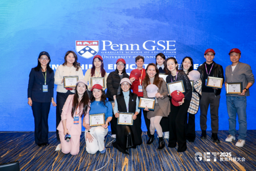 14 students pose for a photo with EdEnt director Jenny Zapf in front of a blue Penn GSE background