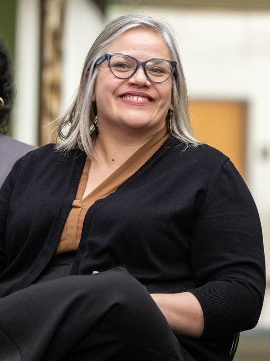 Lauren Overton smiles, wearing glasses and seated in a space in Penn Alexander