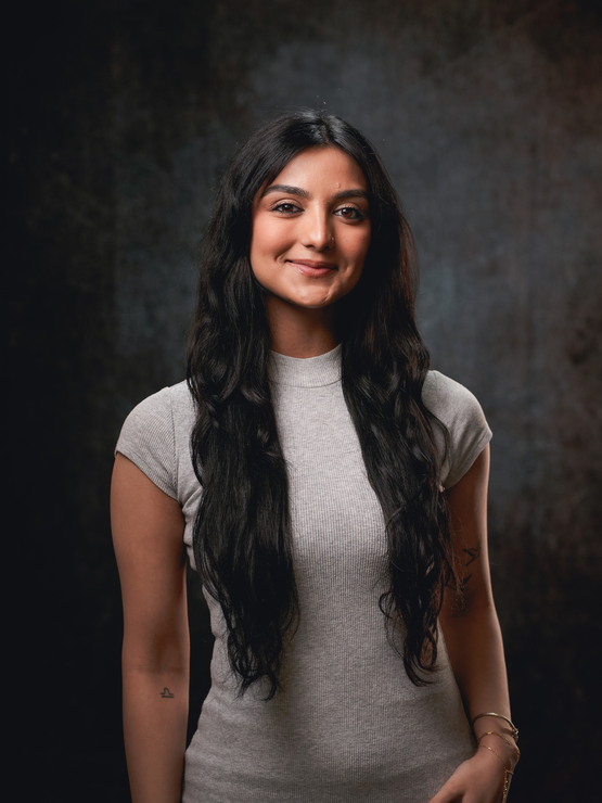 Simran wears a gray dress and smiles against a dark gray background
