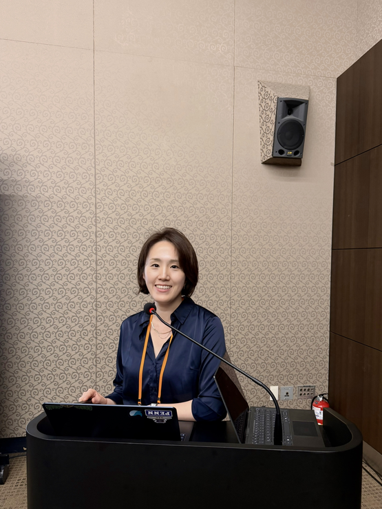 Hyejin Park stands at a podium in front of a microphone smiling.