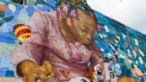 outdoor mural of a little girl reading a book with butterflies, birds, and a hot air balloon rising from the pages