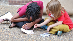 Two children sitting on the sidewalk in front of Penn GSE working on homemade comic books.