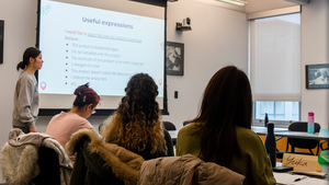 English-as-a-second-language students watch a Penn GSE Educational Linguistics student present a lesson in front of a screen that reads "Useful expressions"