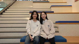Two women in white Penn sweatshirts sit on the stairs in Penn GSE's entrance
