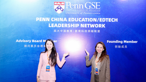 Two alums in China stand in front of a blue background with Penn GSE on it. 