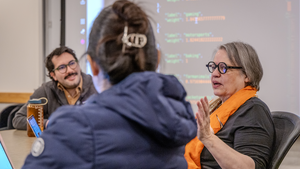 Yasmin Kafai (right) gestures while instructing students around a seminar table in front of a screen displaying computer code.