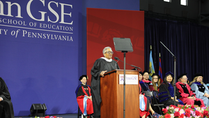EdTrust President and CEO Denise Forte speaks at Penn GSE's 2026 Commencement ceremony, standing on stage at a podium with the faculty seated behind her.