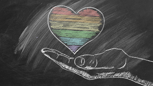 A chalk sketch on a blackboard of a hand held out, palm up, holding a heart with a six-stripe rainbow representing LGBTQ+ pride.
