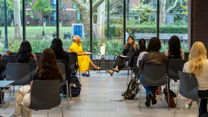 Marsha Richardson and Neerja Birla sit facing each other in front of a wall of windows in front of an audience of students